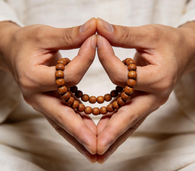 Hands holding wooden mala beads in traditional meditation counting position with beads wrapped around fingers