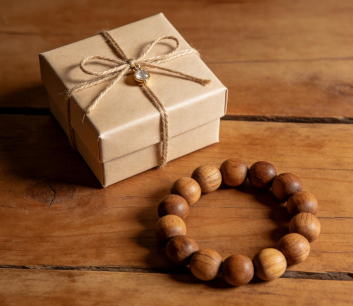 Wrapped jewelry gift box on wooden surface with loose sandalwood mala beads