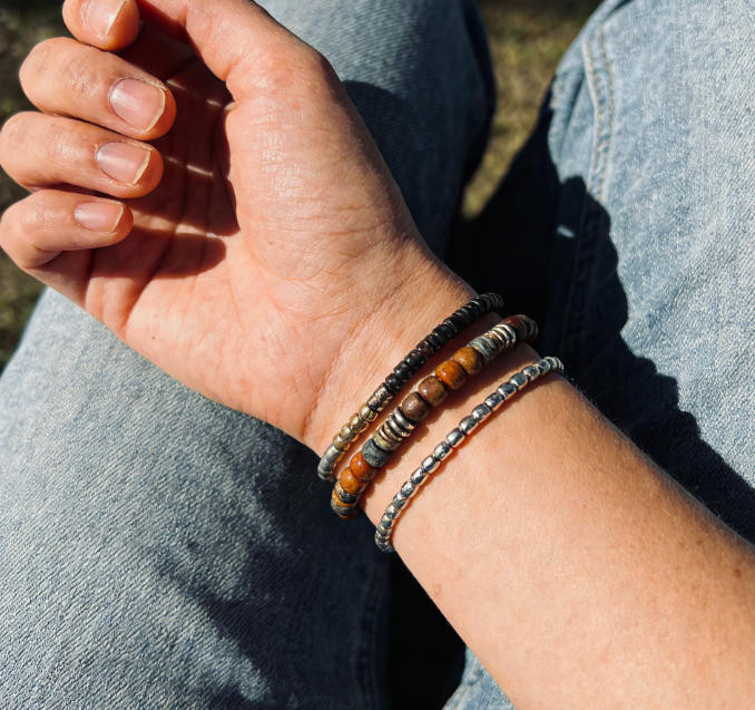 Wrist wearing three stacked bracelets: wooden mala beads, jade bracelet, and thin gold bangle